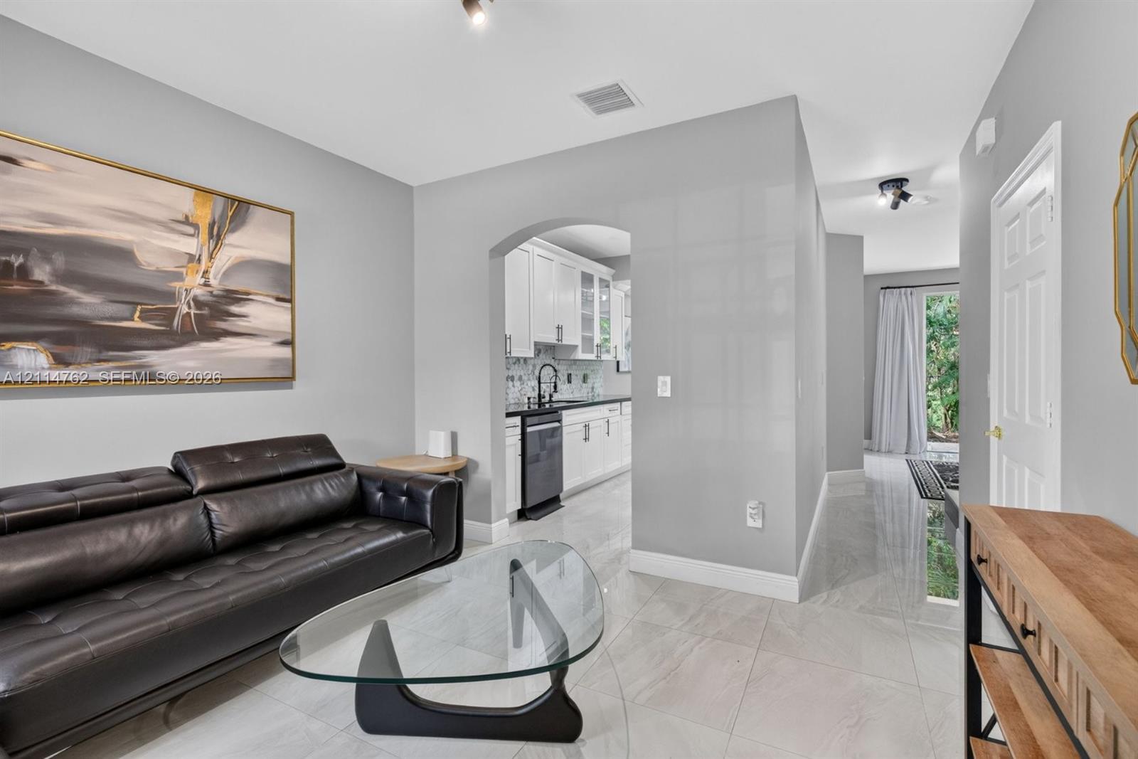 Interior featuring polished stone-look tile flooring, arched entryway, and white kitchen cabinetry with high-contrast dark countertops