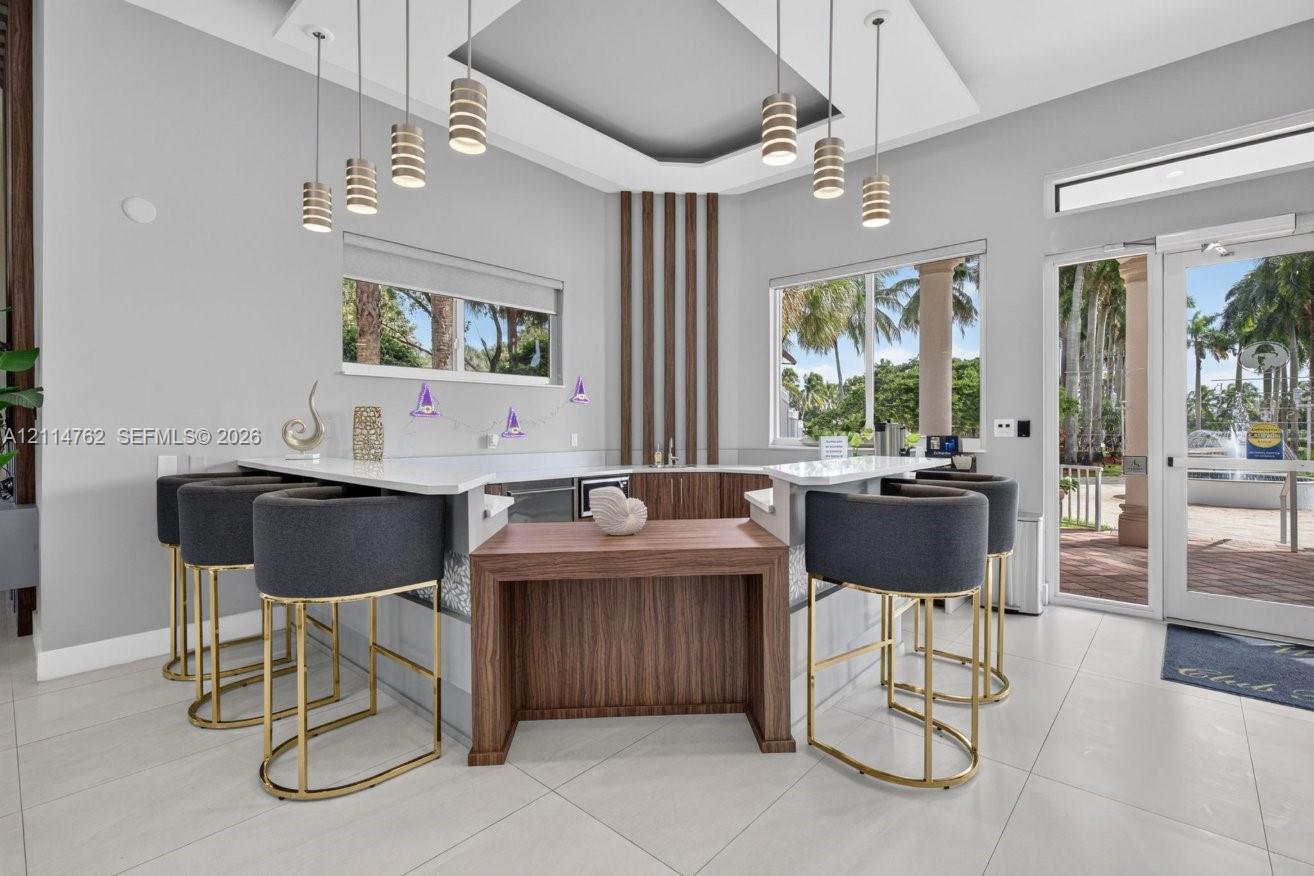 Built-in wet bar featuring custom wood-finish cabinetry, stone-surface countertops, tiered multi-level workspace, and cylindrical pendant lighting suspended from a tray ceiling