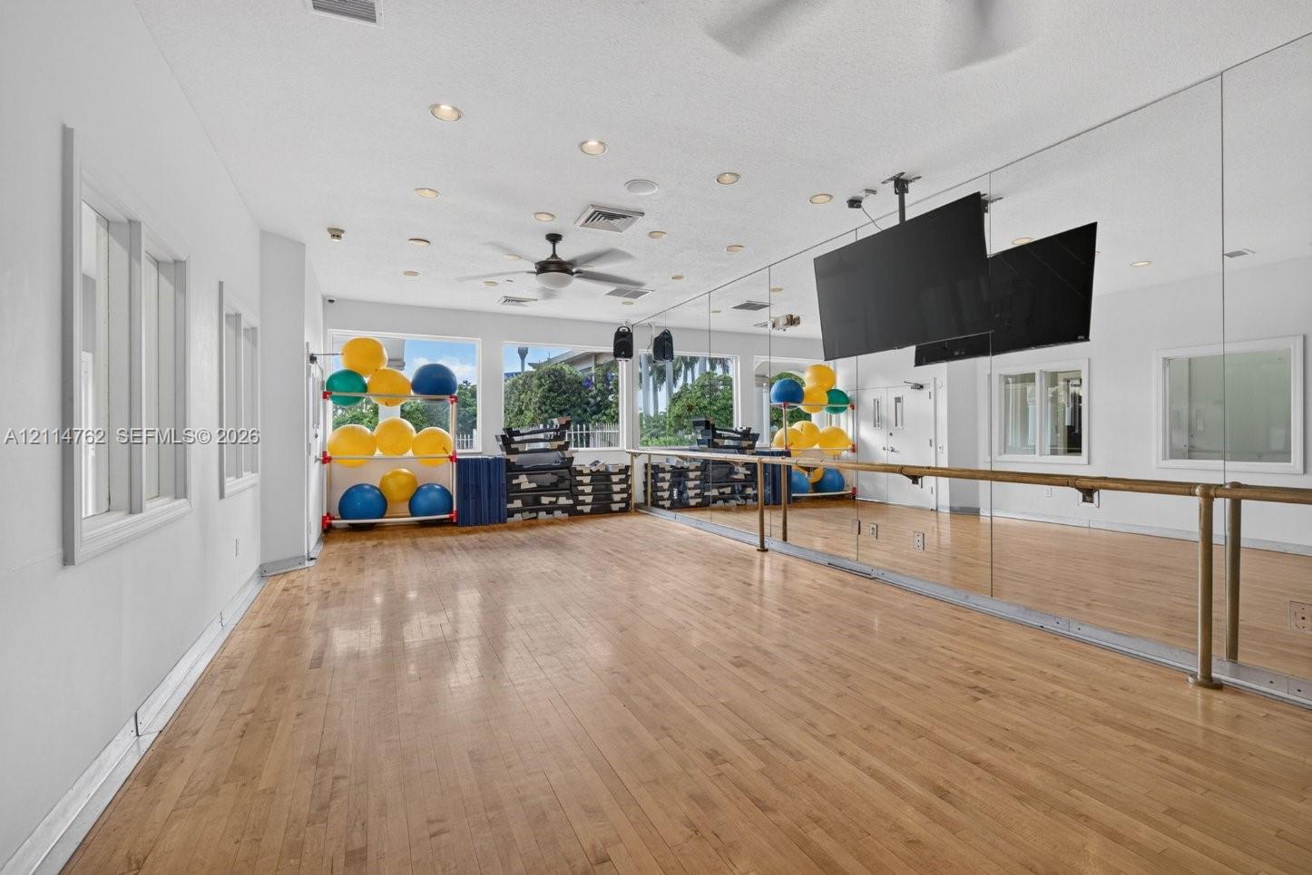 Spacious room featuring wood-finish flooring, full-length wall mirrors, a mounted ballet barre, recessed lighting, and a ceiling fan