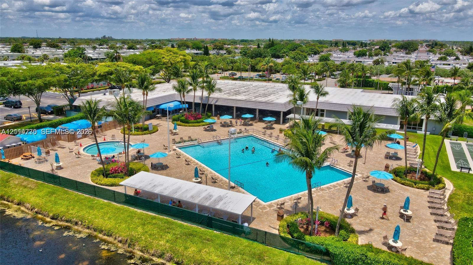 Outdoor recreation area featuring a large swimming pool, circular spa, paved terrace, covered pavilion, and mature palm trees