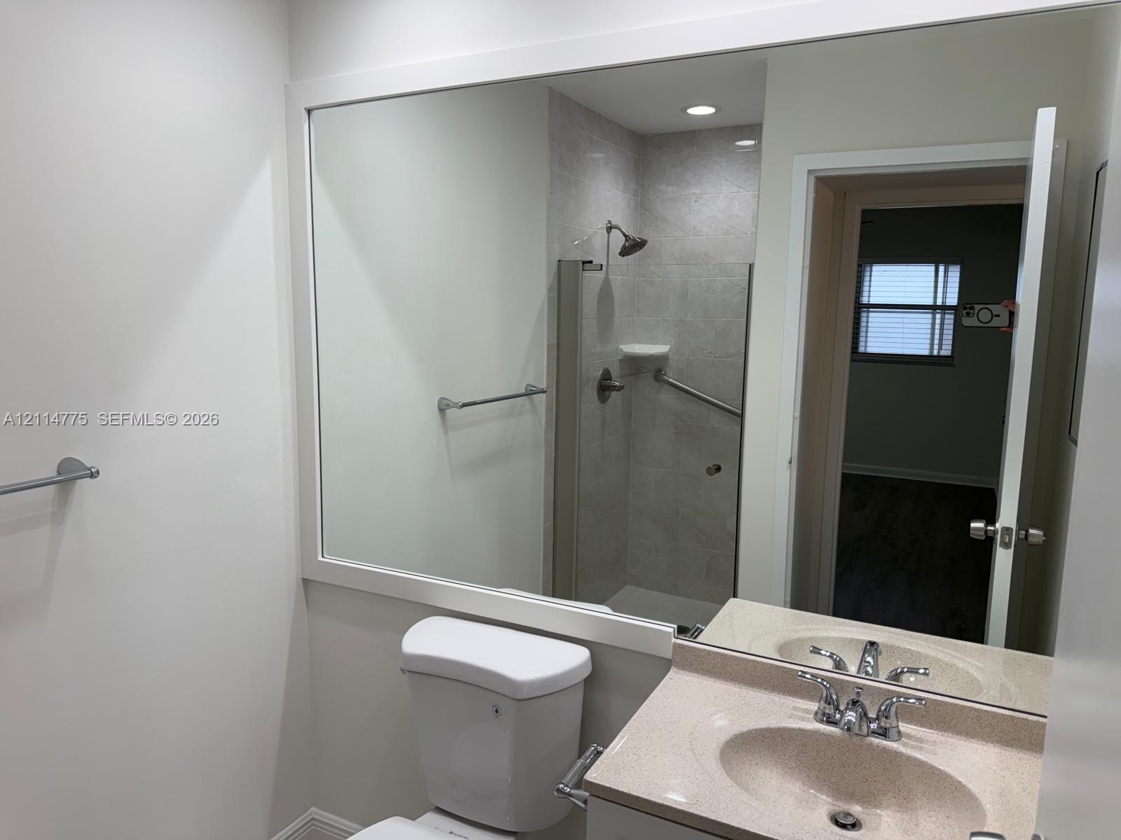Bathroom featuring a vanity with a solid-surface countertop, an integrated sink, a large wall-mounted mirror, and a walk-in shower with stone-finish wall tile
