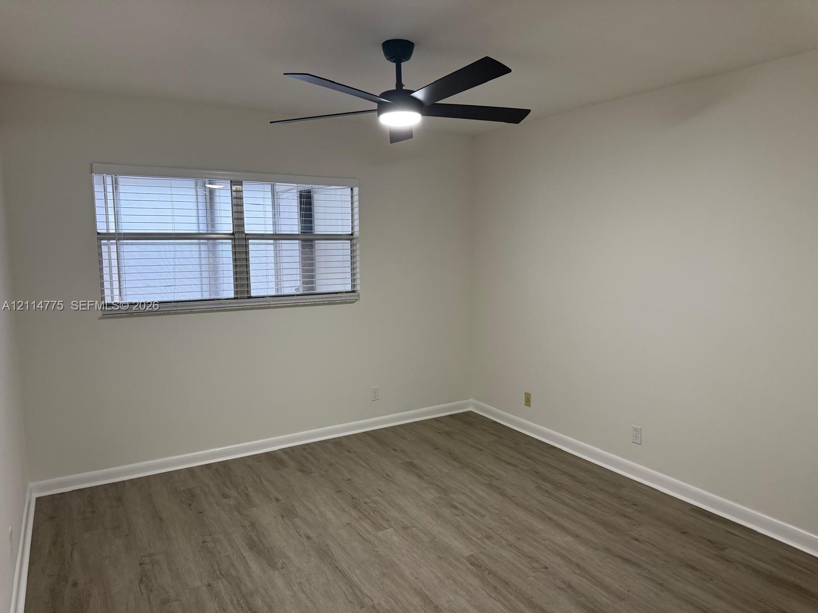 Room featuring wood-finish flooring, a matte black ceiling fan with integrated lighting, and a multi-pane window with installed blinds