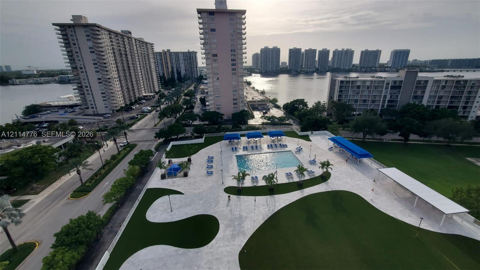 Outdoor swimming pool with integrated hardscaping, stone-paved deck, manicured green space, and covered cabana areas