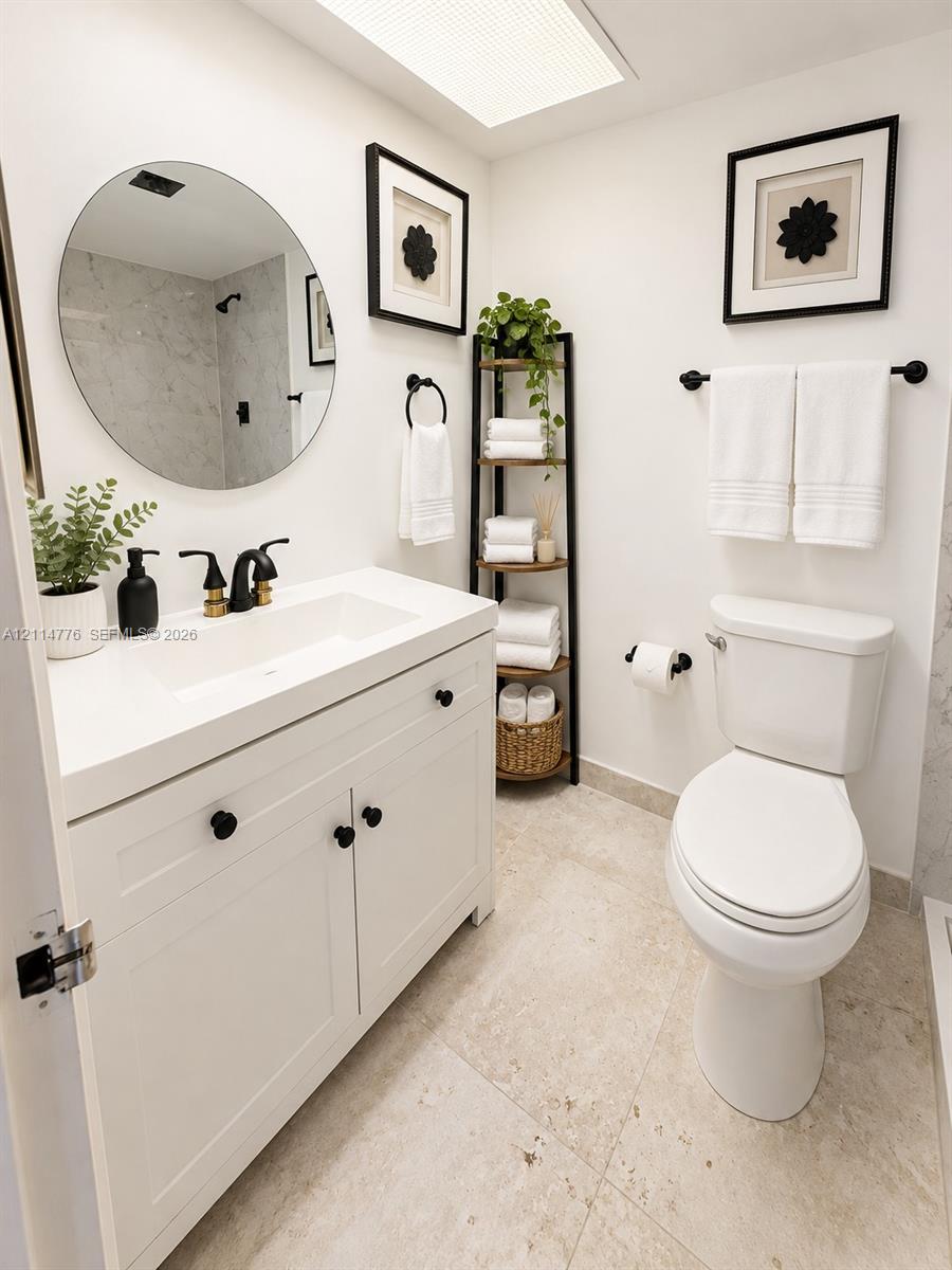 Bathroom featuring a white vanity with an integrated rectangular sink and stone-surface countertop, circular frameless wall mirror, matte black plumbing fixtures, and natural stone flooring