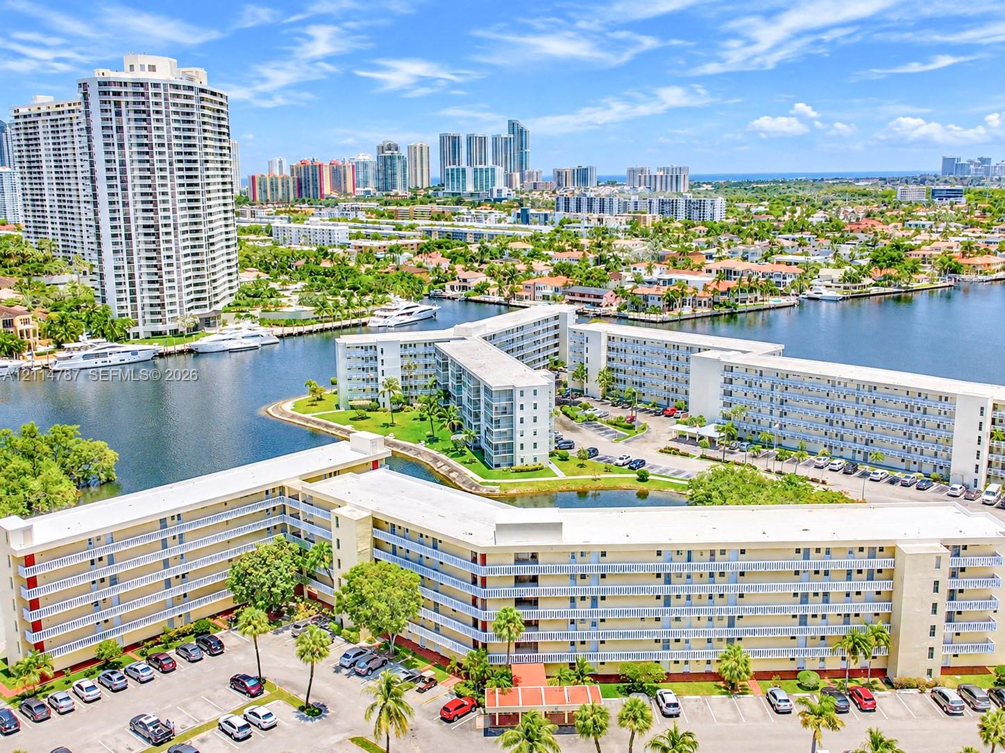 Waterfront multi-story residential complex featuring landscaped grounds, exterior balconies, and surface parking areas