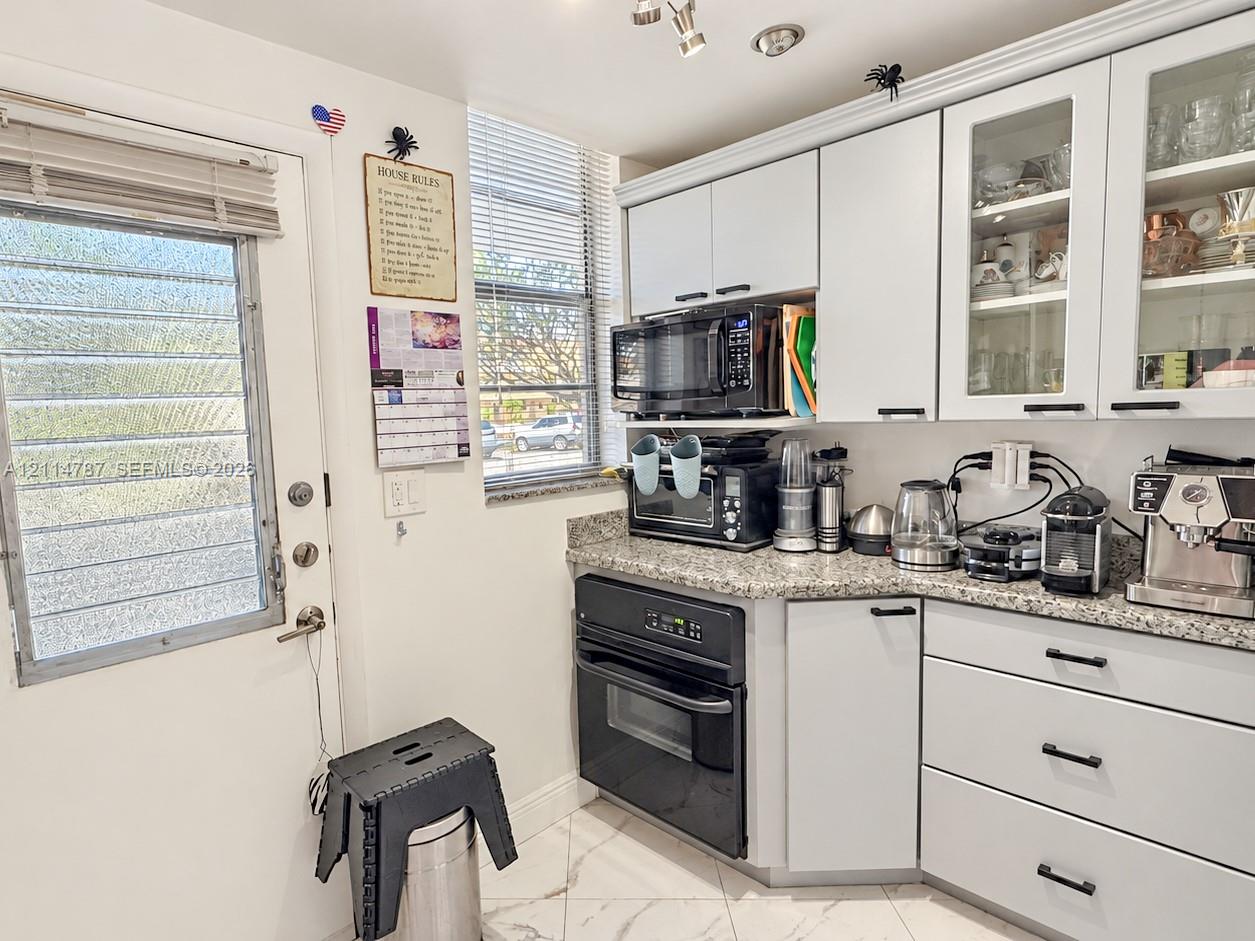 Kitchen featuring white cabinetry with glass-front uppers, speckled stone countertops, black integrated oven, built-in microwave, and tile flooring