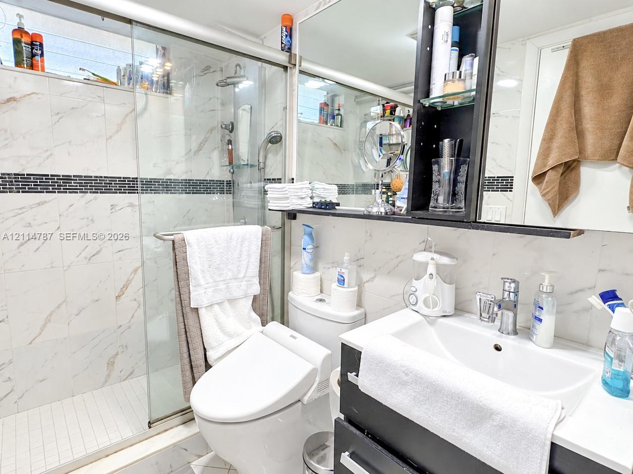 Bathroom featuring a glass-enclosed shower, stone-finish wall tile with mosaic accent inlay, built-in medicine cabinet, and a vanity with a white countertop and integrated sink