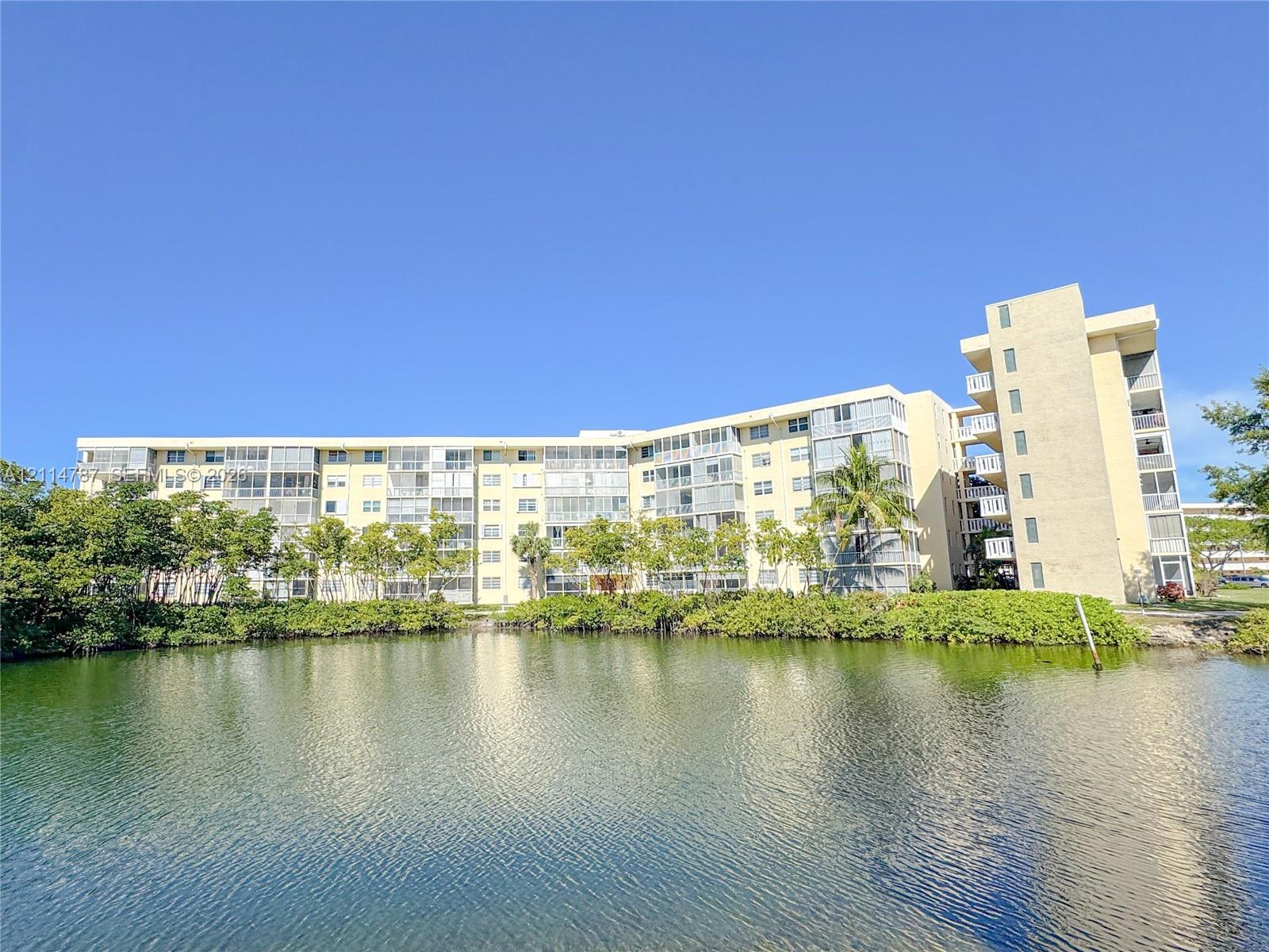 Multi-story residential building featuring private screened balconies, exterior facade with neutral finish, and a prominent water feature with landscaped vegetation
