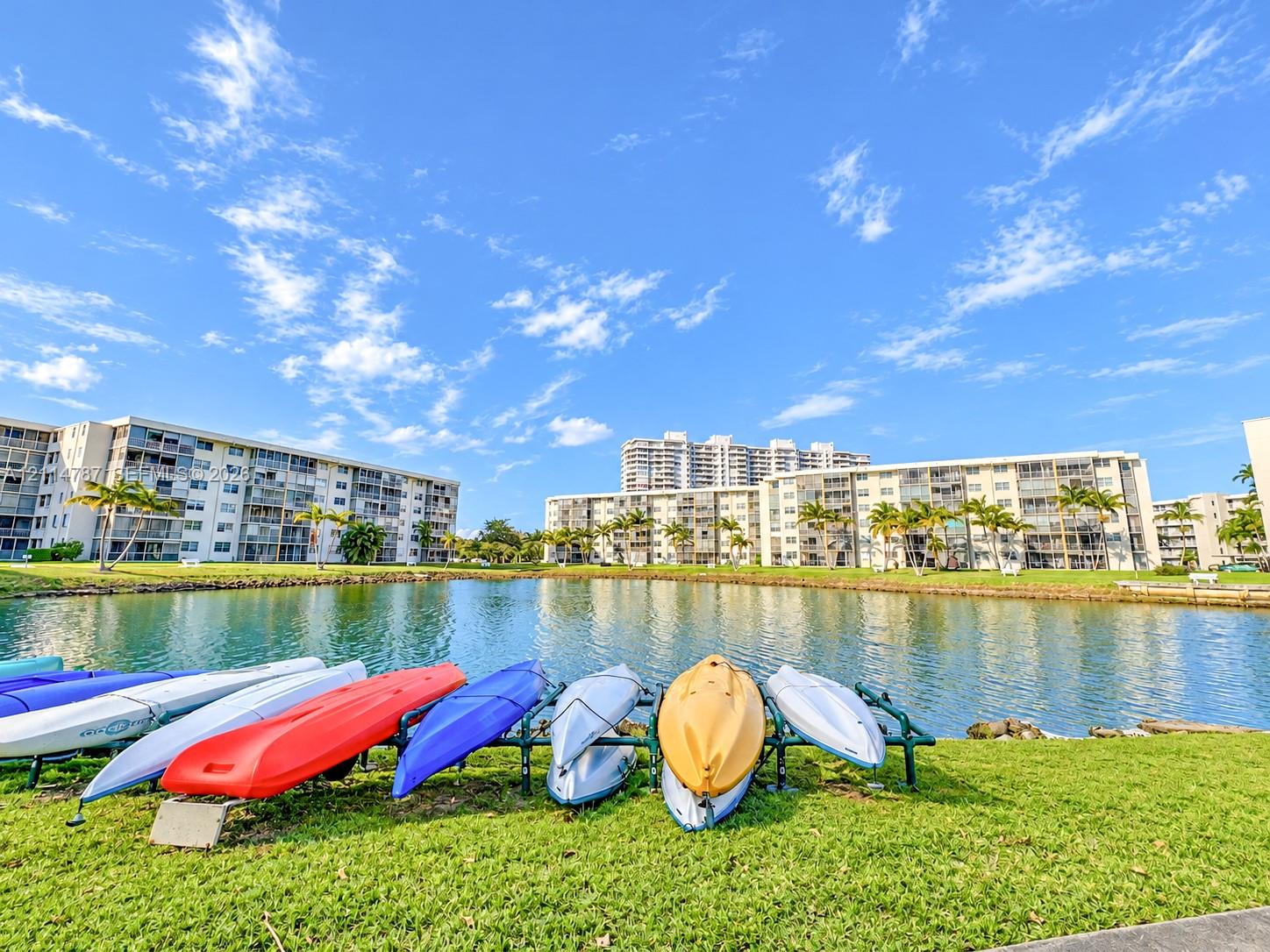 Waterfront community grounds featuring a central pond, established palm trees, landscaped lawn, and a dedicated kayak rack