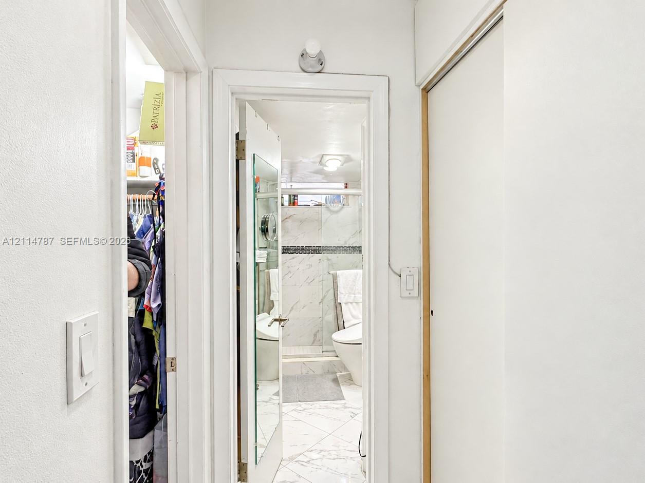 Bathroom featuring stone-finish wall and floor tiling, a glass-enclosed shower, a wall-mounted light fixture, and floor-to-ceiling closet cabinetry
