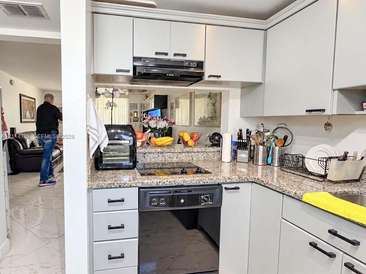 Kitchen featuring light-toned flat-panel cabinetry, stone-patterned countertops, a black glass-top range, and a built-in range hood