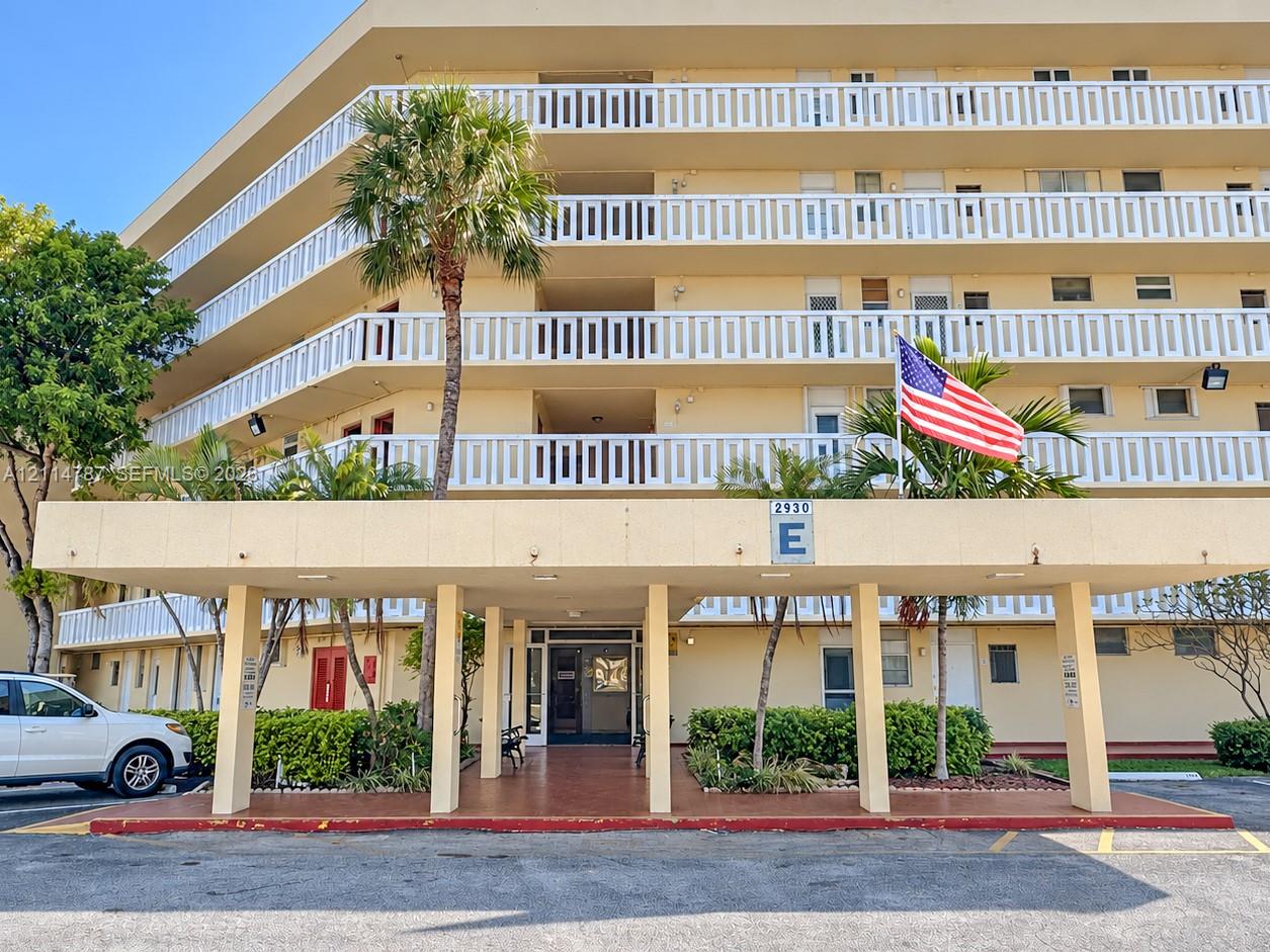 Multi-story exterior featuring a covered porte-cochre, decorative balcony railings, masonry construction, and mature palm trees
