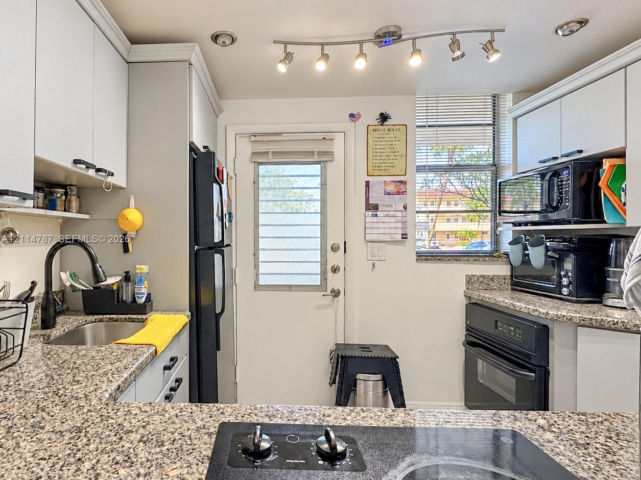 Kitchen featuring speckled stone countertops, shaker-style cabinetry, a built-in oven, a black gooseneck faucet, and multi-light track lighting