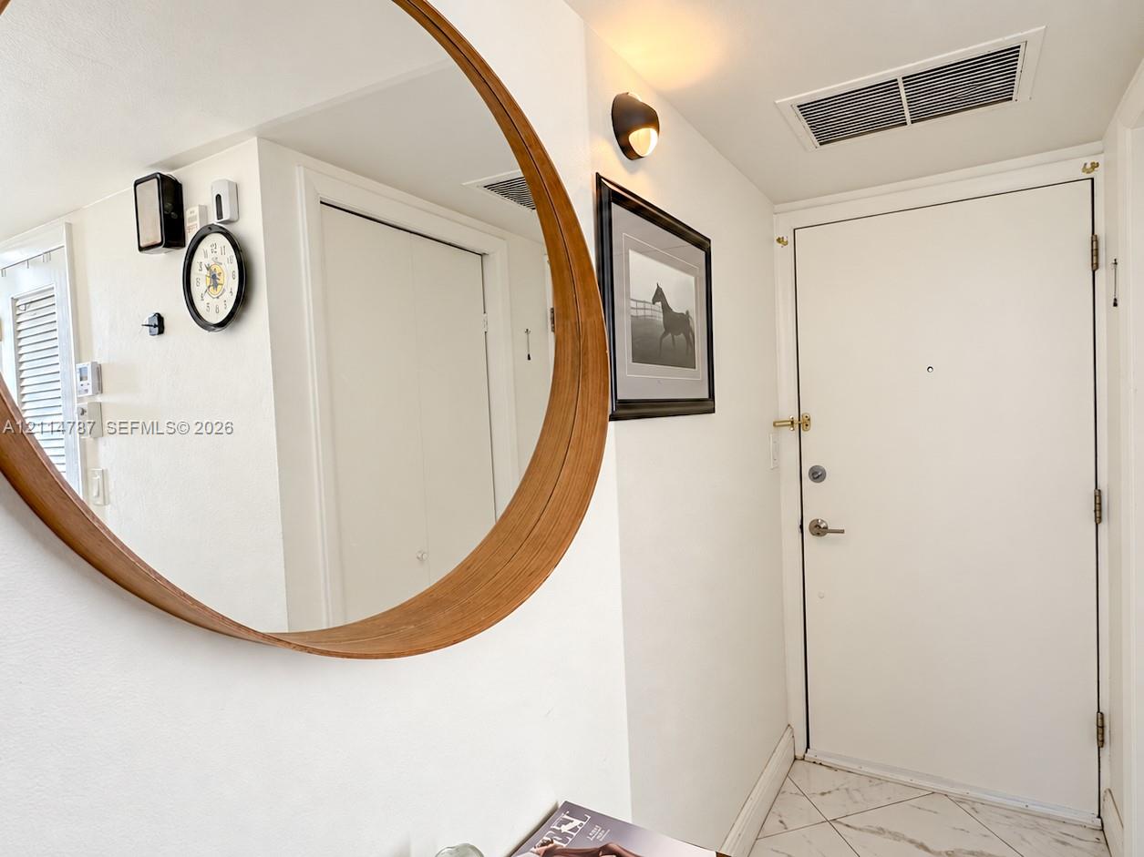 Circular wall mirror with a wood-finish frame, solid-core interior door with metallic hardware, and white tile flooring