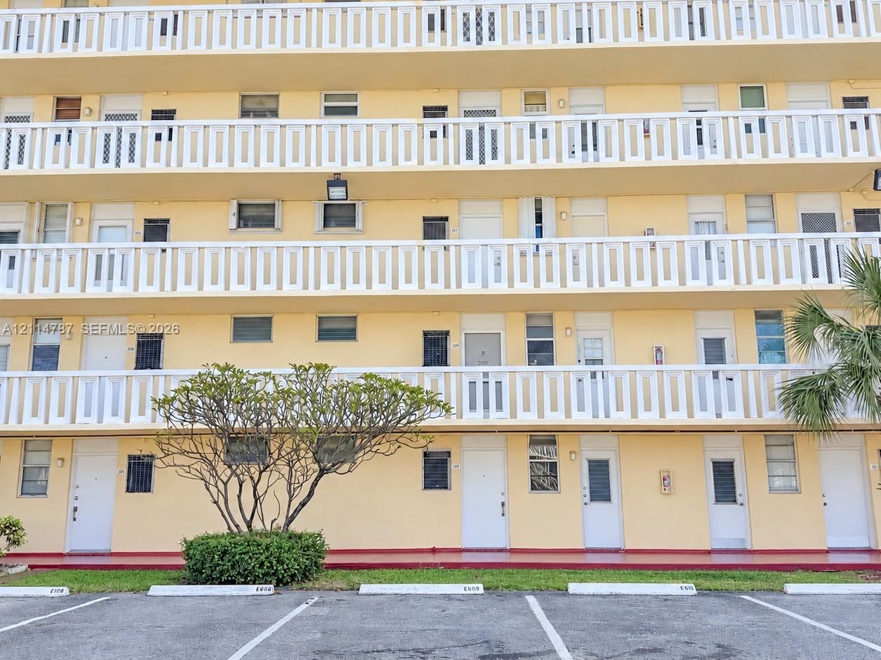 Multi-story exterior featuring continuous white balcony railings, uniform entry doors, and ground-level parking spaces