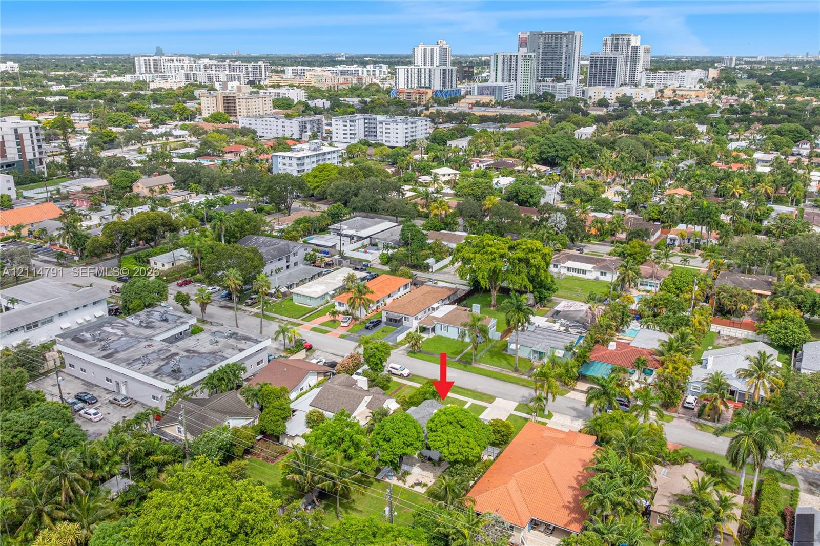 Aerial perspective showcasing a residential property with established landscaping and mature trees, situated within a coastal urban area featuring paved street access
