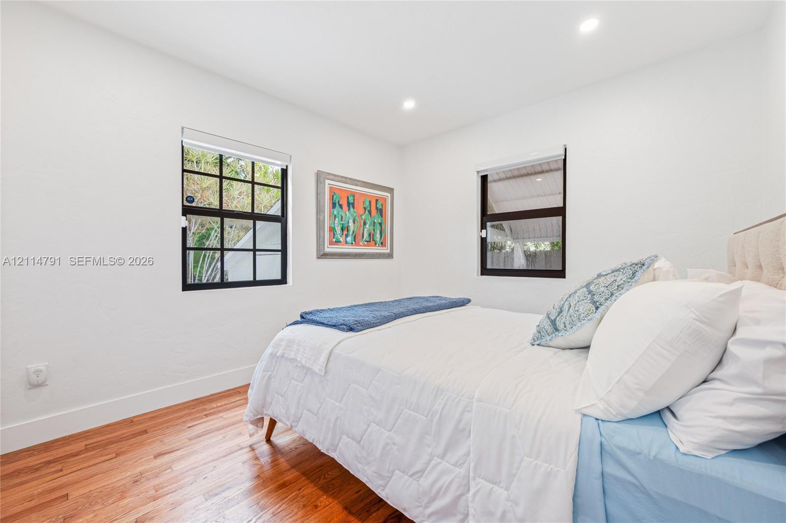Neutral-toned room featuring wood-finish flooring, dual windows with black frames, and recessed lighting