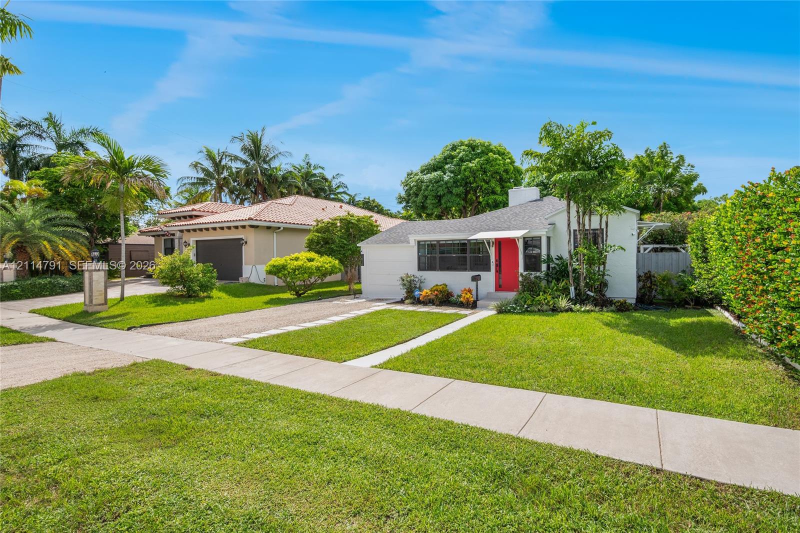 Single-story residence featuring a painted stucco exterior, high-contrast front entry door, metal awning over the entryway, and a paved driveway