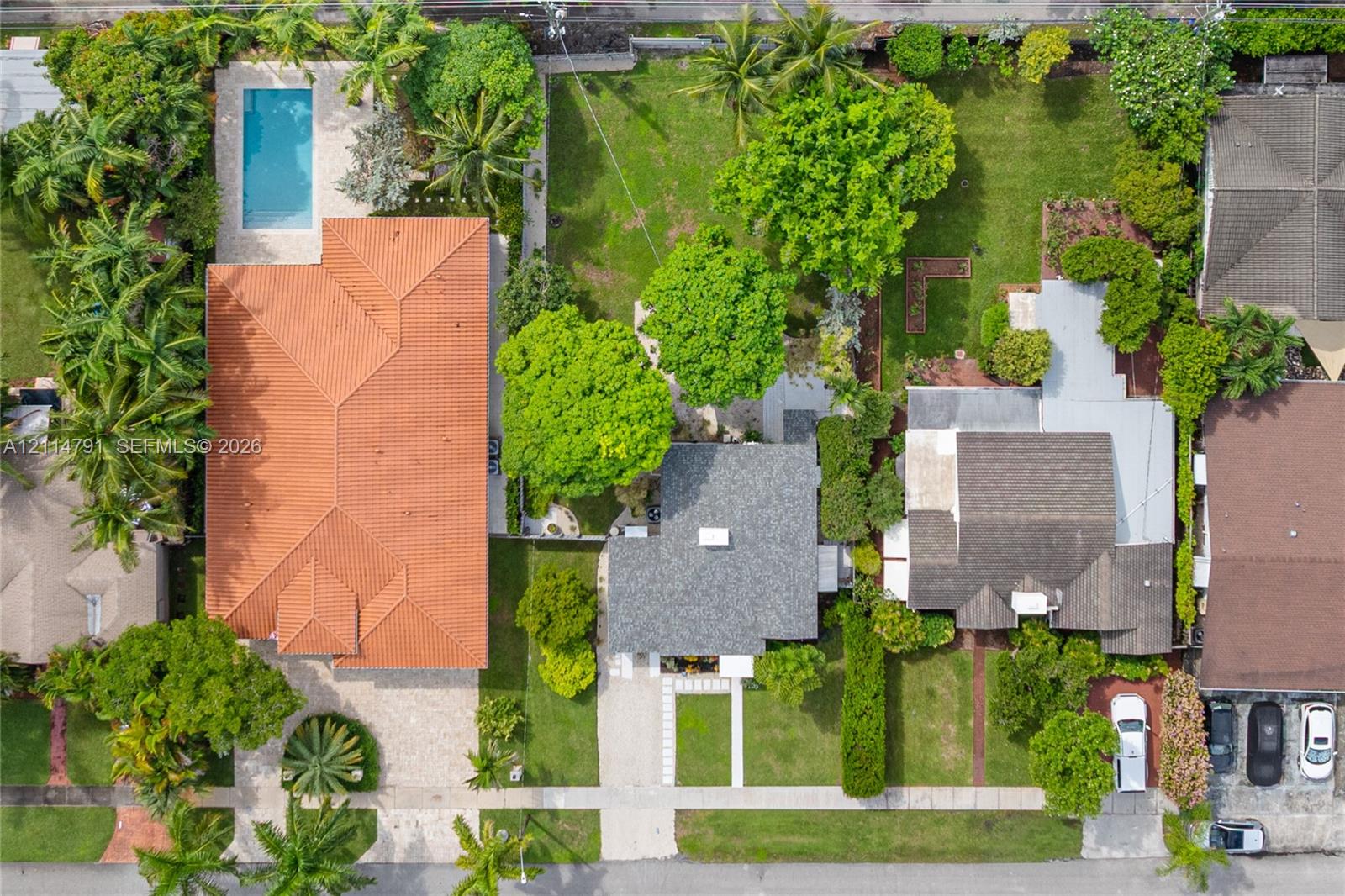 Aerial perspective featuring a terracotta tile roof, rectangular swimming pool, expansive green space, mature landscaping, and concrete driveway