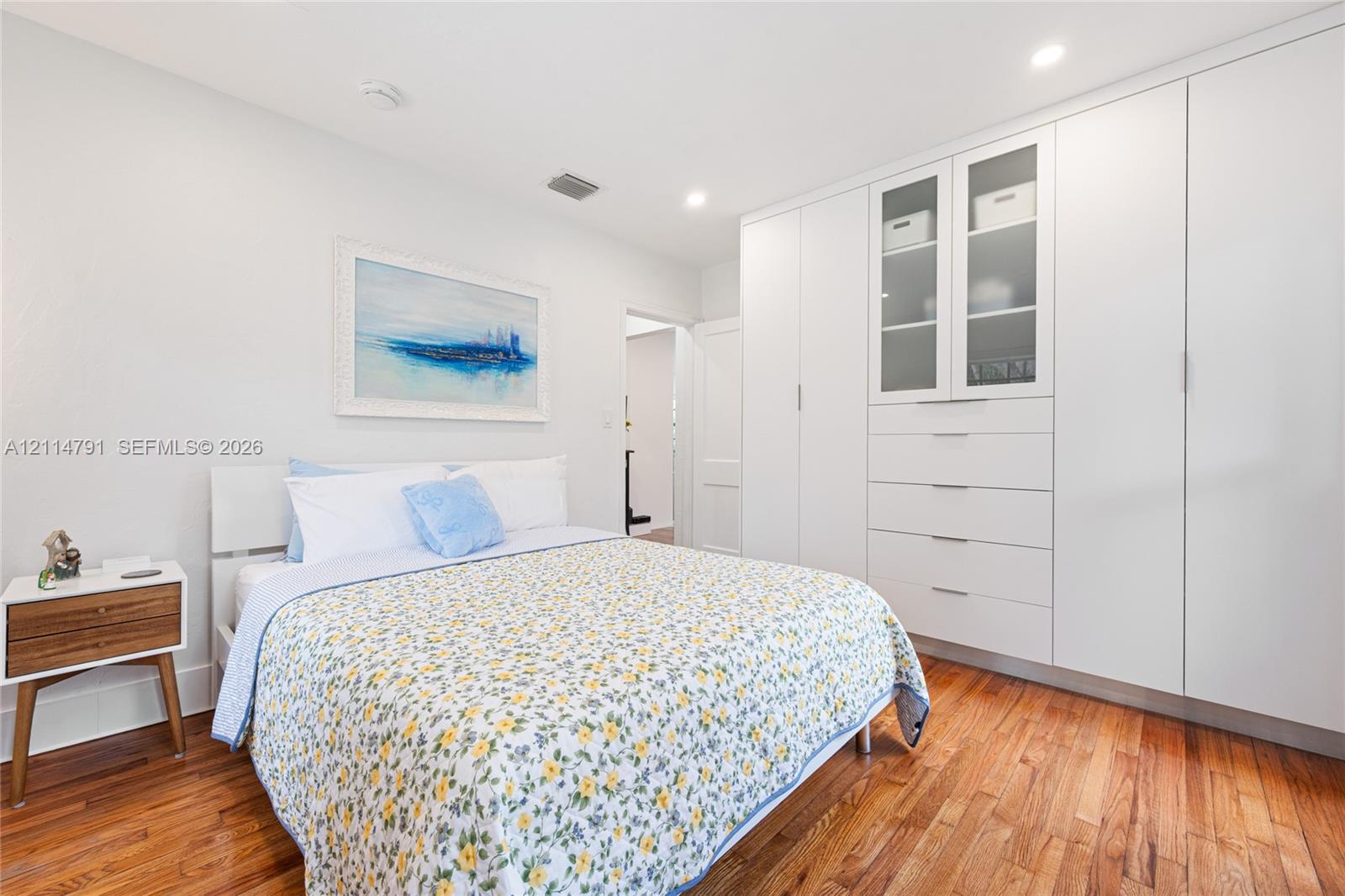 Floor-to-ceiling white cabinetry with integrated drawers and glass-front display shelving, wood-finish flooring, and recessed ceiling lighting