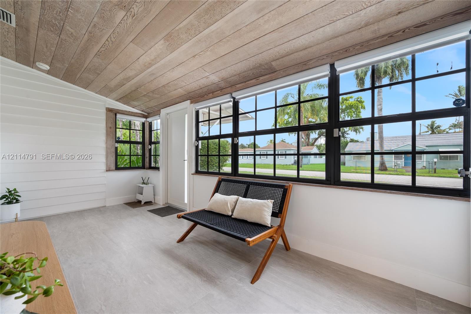 Sunroom featuring a natural wood-finish plank ceiling, horizontal shiplap wall paneling, expansive black-framed multi-pane windows, and light-toned flooring
