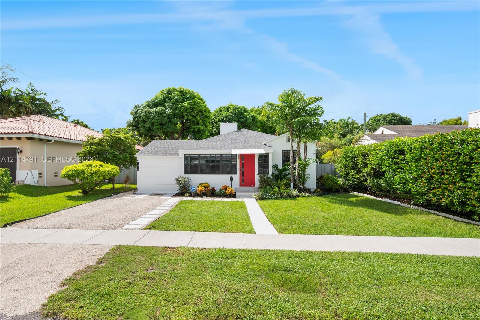 Single-story residence featuring a white stucco exterior, asphalt shingle roof, vibrant red front door, gravel driveway, and a manicured front lawn
