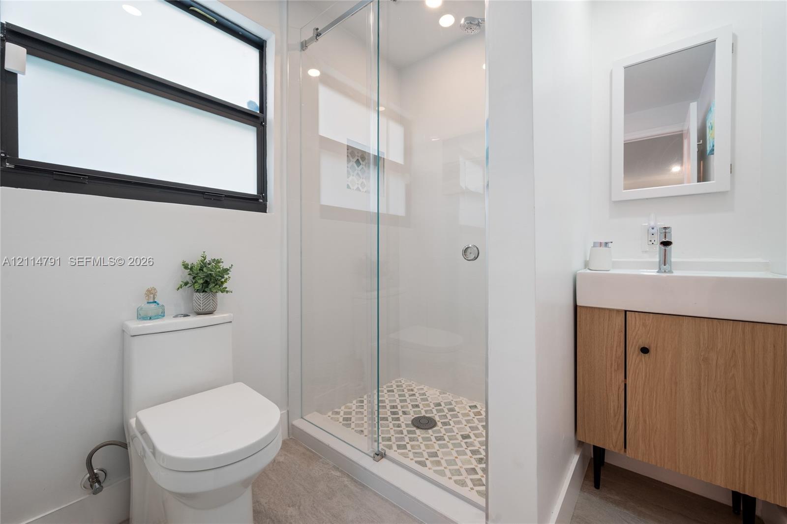 Walk-in glass enclosed shower with decorative tile flooring, wall-mounted vanity with integrated sink, and horizontal transom window