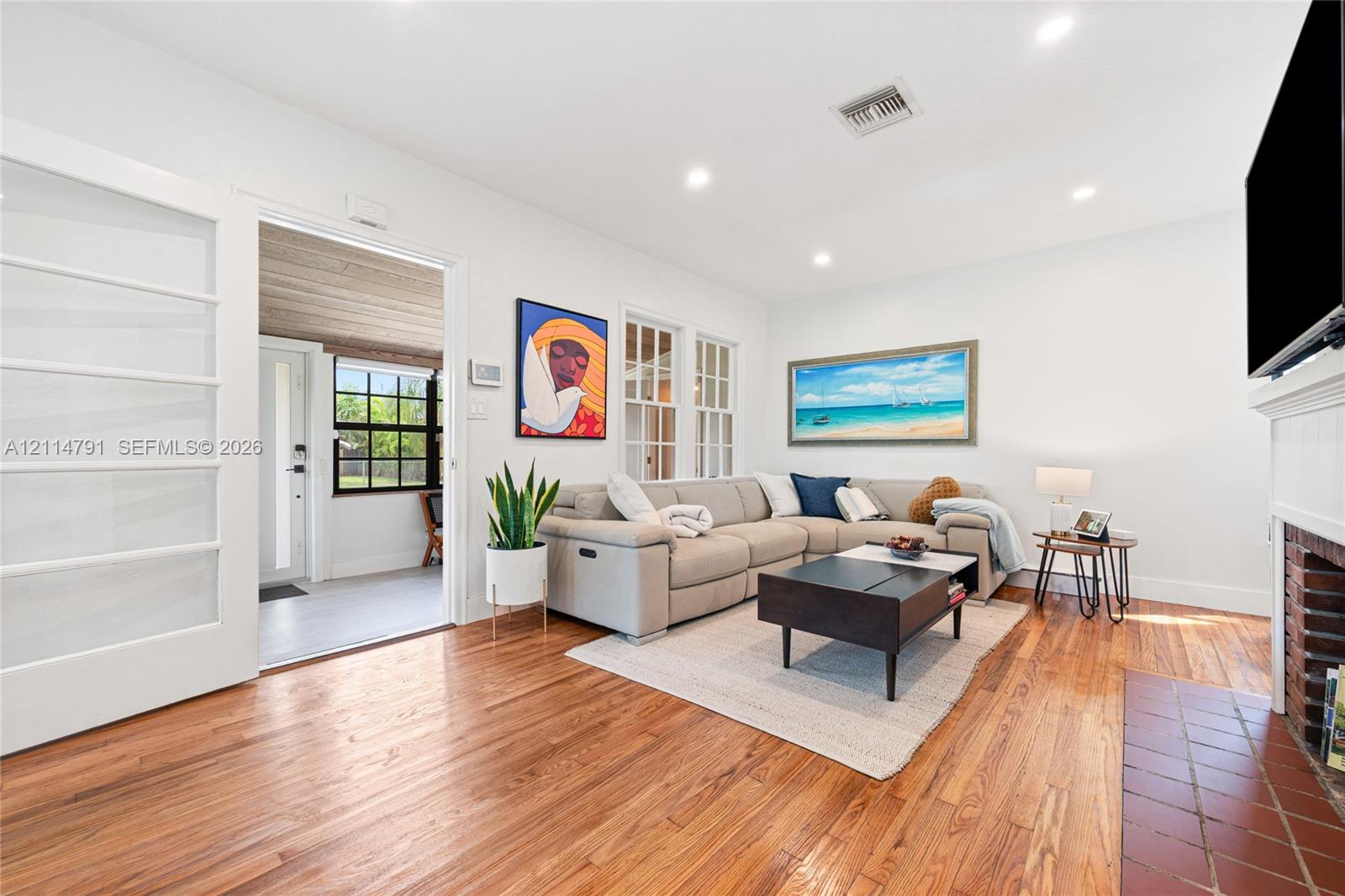Living area featuring wood-finish flooring, recessed lighting, a fireplace with a brick surround, and French doors with glass panes