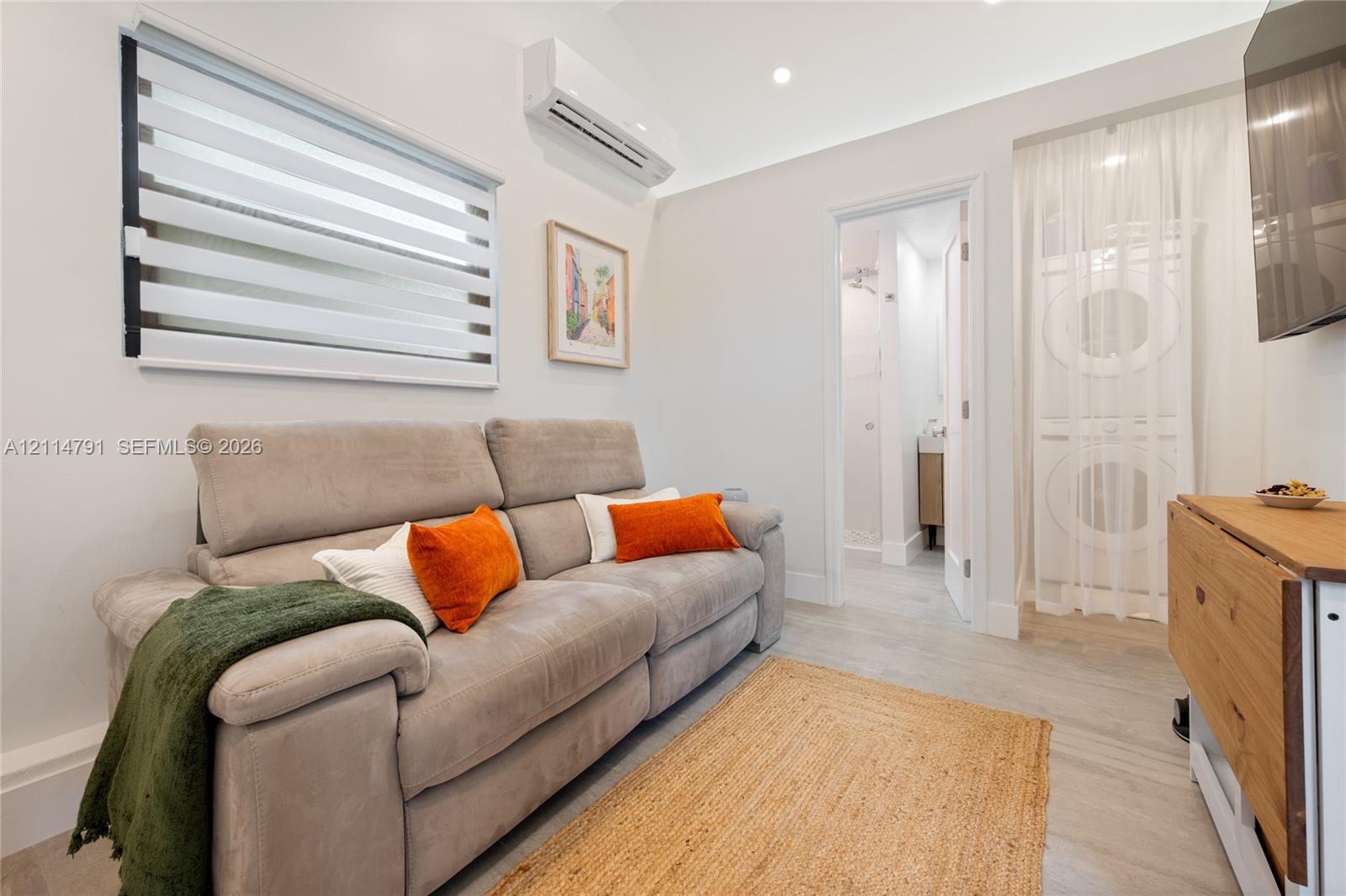 Wall-mounted HVAC unit, recessed lighting, dual-roller window shade, and stacked laundry unit concealed by sheer drapery