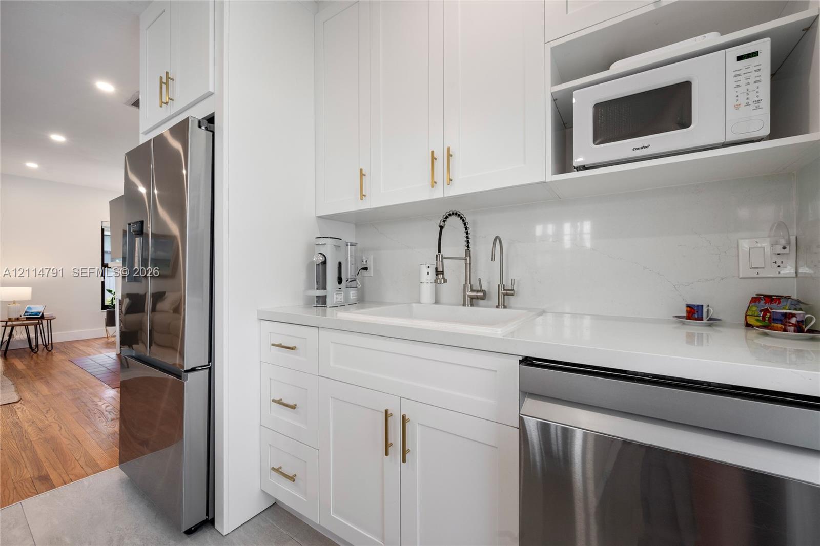 Kitchen featuring white Shaker-style cabinetry with gold-tone pulls, stone-composite countertops, integrated farmhouse sink with a gooseneck faucet, and stainless steel appliances