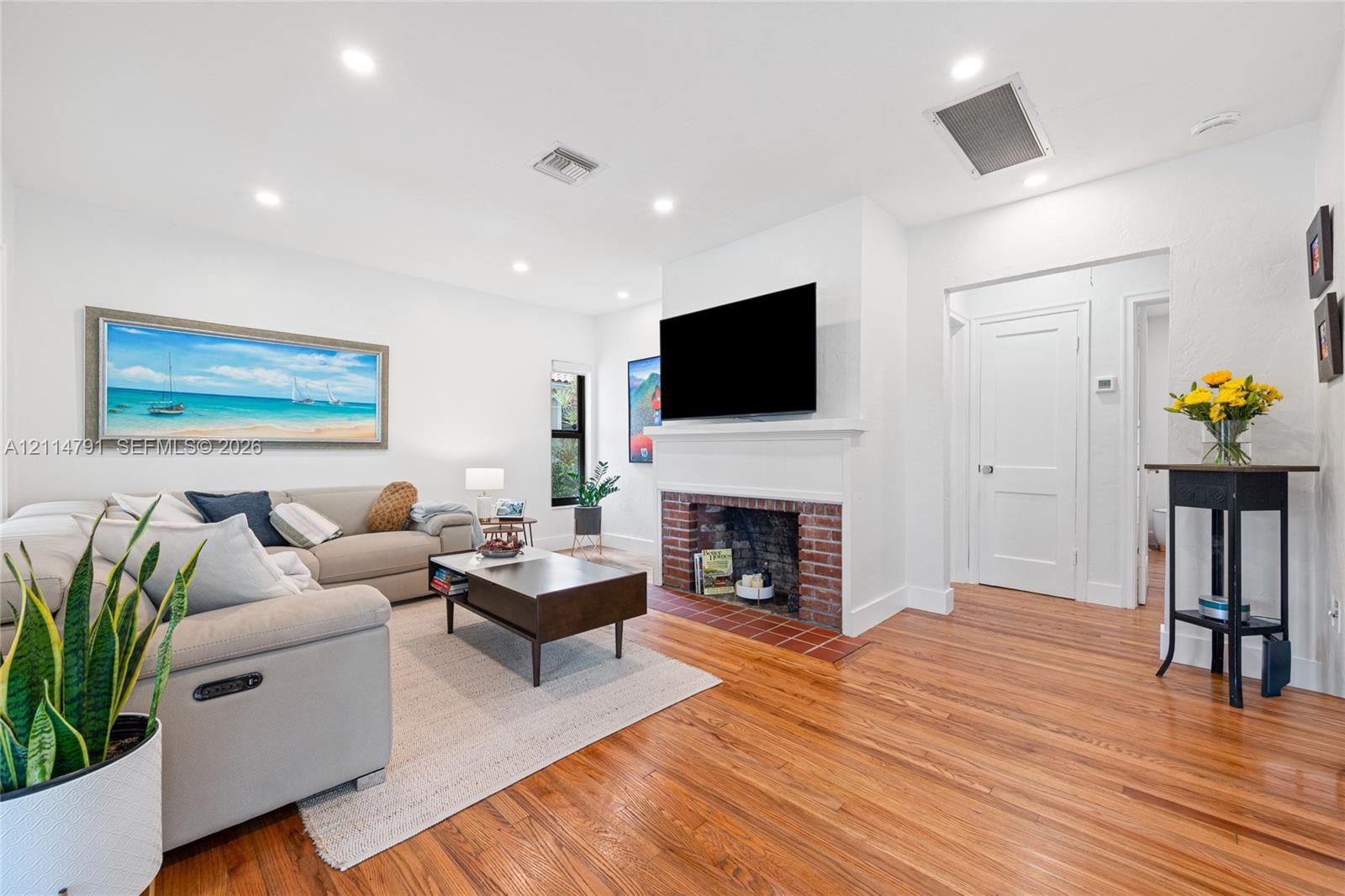 Living area featuring hardwood flooring, a masonry fireplace with a brick surround, recessed lighting, and a white mantle
