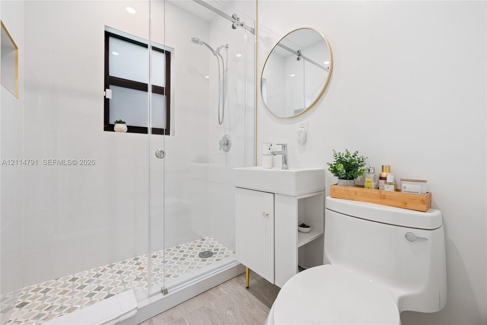 Bathroom featuring a walk-in shower with glass enclosure, decorative mosaic tile flooring, floating vanity with vertical detailing, and a circular wall-mounted mirror