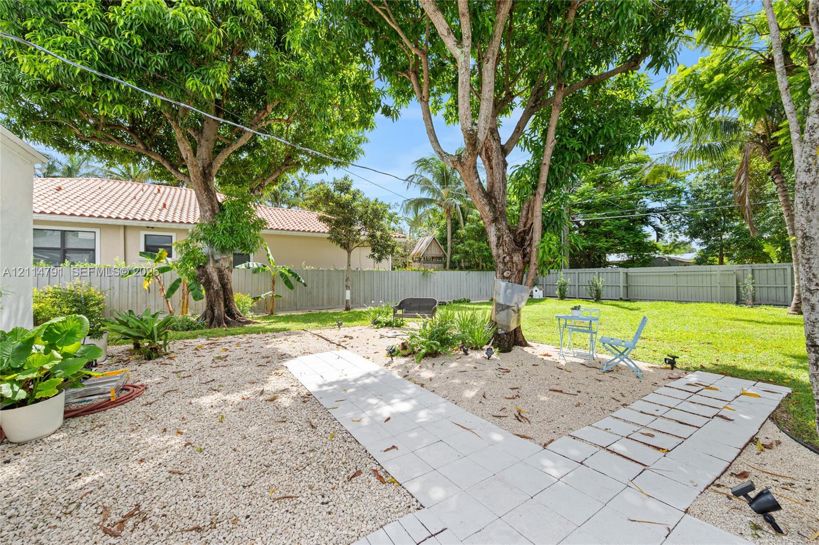 Backyard featuring a paved stone walkway, crushed stone ground cover, mature shade trees, a manicured lawn, and perimeter fencing