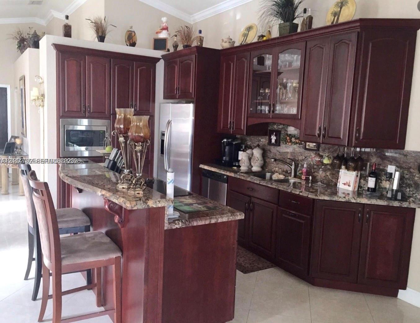 Kitchen featuring dark wood cabinetry, a breakfast bar, stone-patterned countertops, stainless steel appliances, and glass-front upper cabinet doors