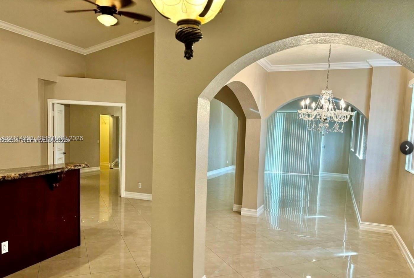 Interior featuring high ceilings, neutral wall tones, polished tile flooring, decorative arched architectural details, and crystal-style chandelier lighting