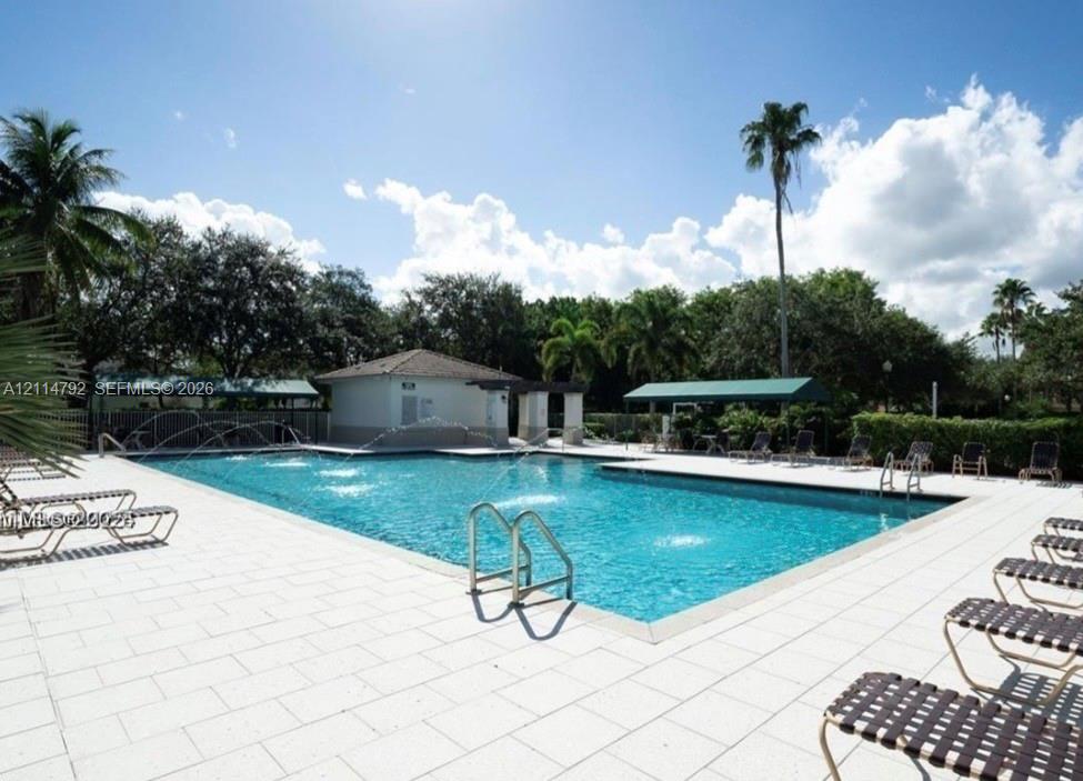 Swimming pool featuring water fountains, tiled decking, a shaded cabana, and mature perimeter landscaping
