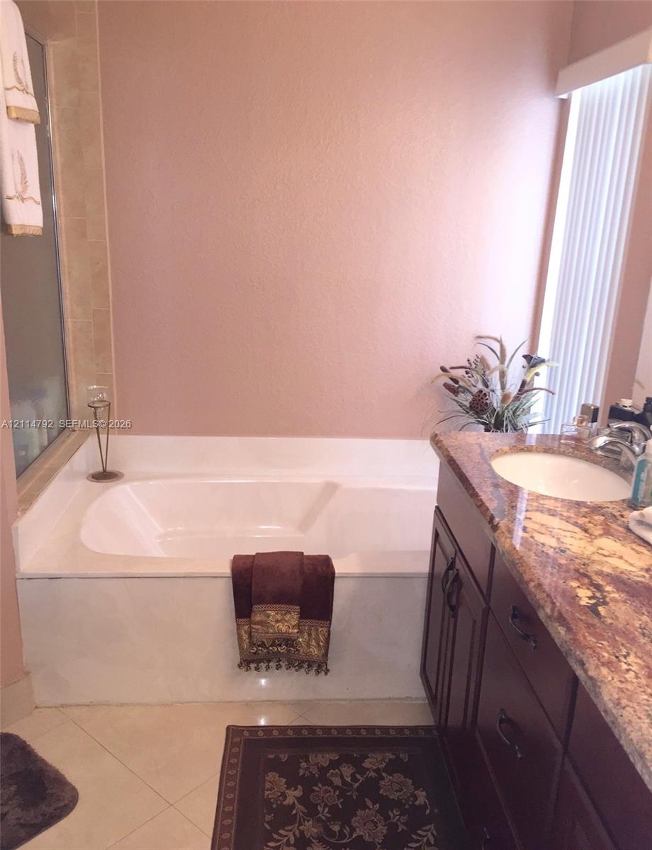 Deep soaking tub with a tile surround, vanity with stone countertop, and an undermount sink