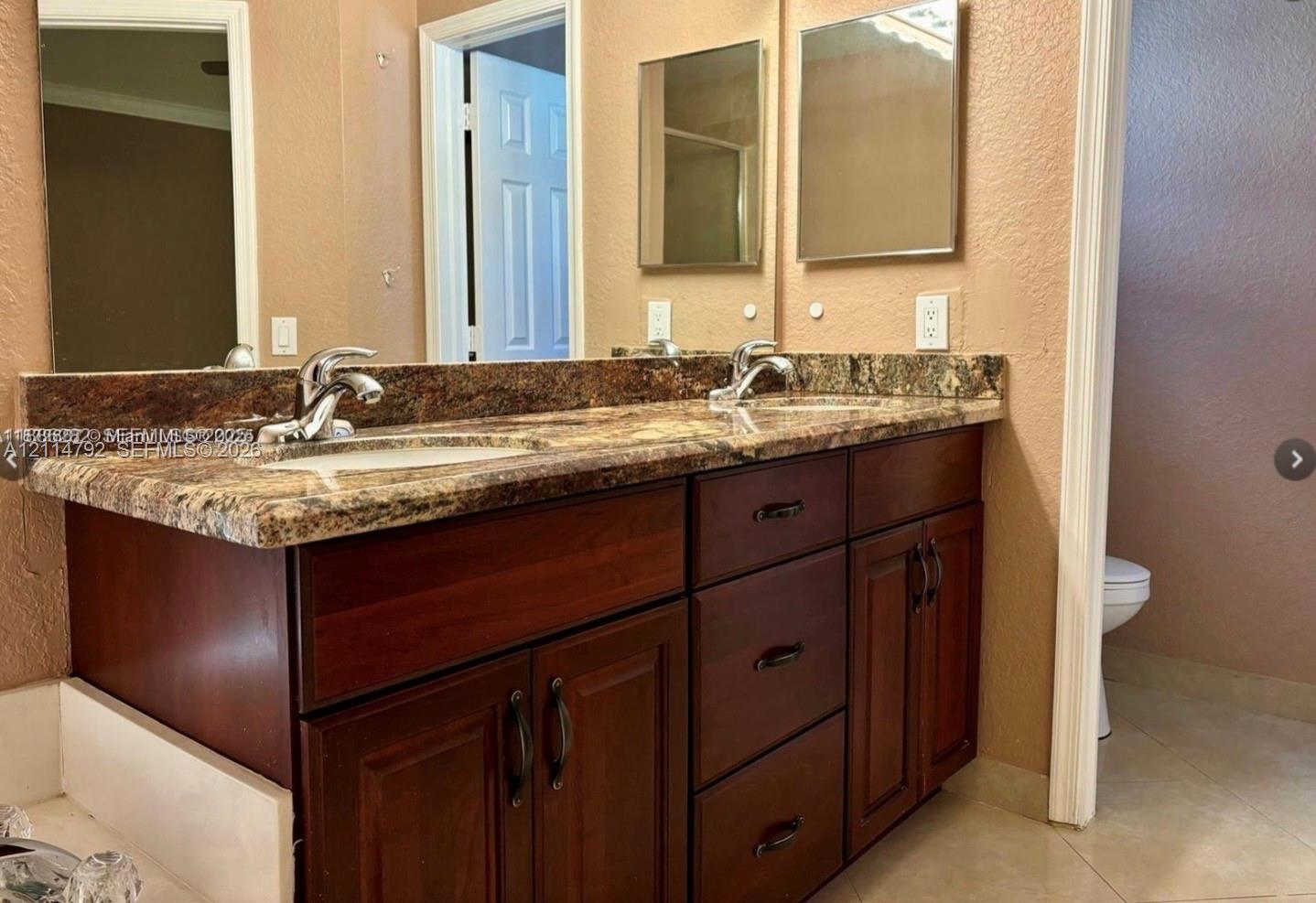 Double-sink vanity featuring dark wood-finish cabinetry, stone-patterned countertops, dual undermount basins with polished chrome faucets, and two wall-mounted mirrors