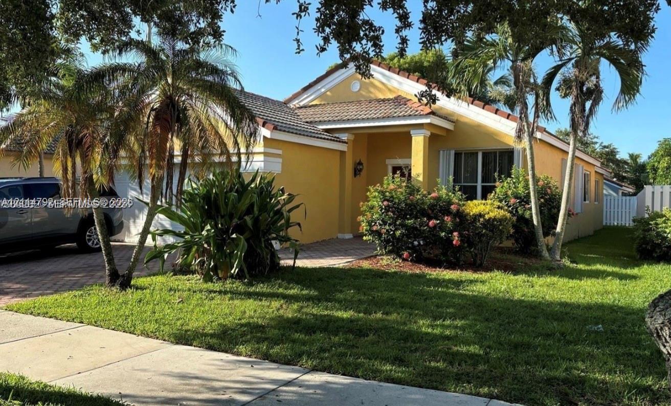 Single-story residence featuring a paved driveway, tiled roof, stucco exterior, covered entryway, and mature palm trees
