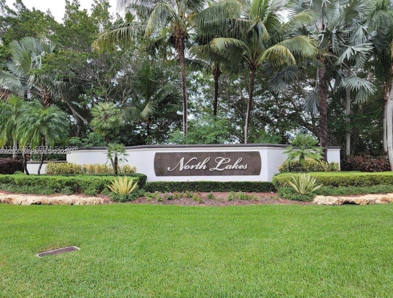 Community monument sign featuring a curved masonry wall, decorative stone inlay, and manicured landscaping with mature palm trees