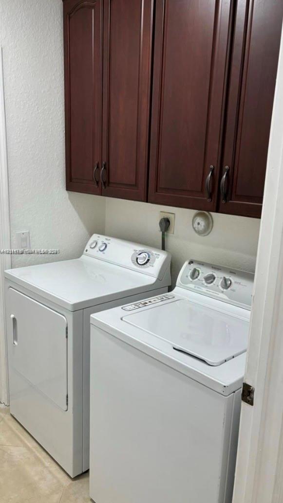 Laundry area featuring elevated dark wood-finish cabinetry and neutral tile flooring
