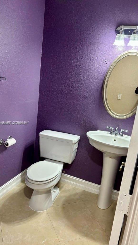 Pedestal sink with dual-handle chrome faucet, oval wall-mounted mirror, two-piece toilet, and tile flooring