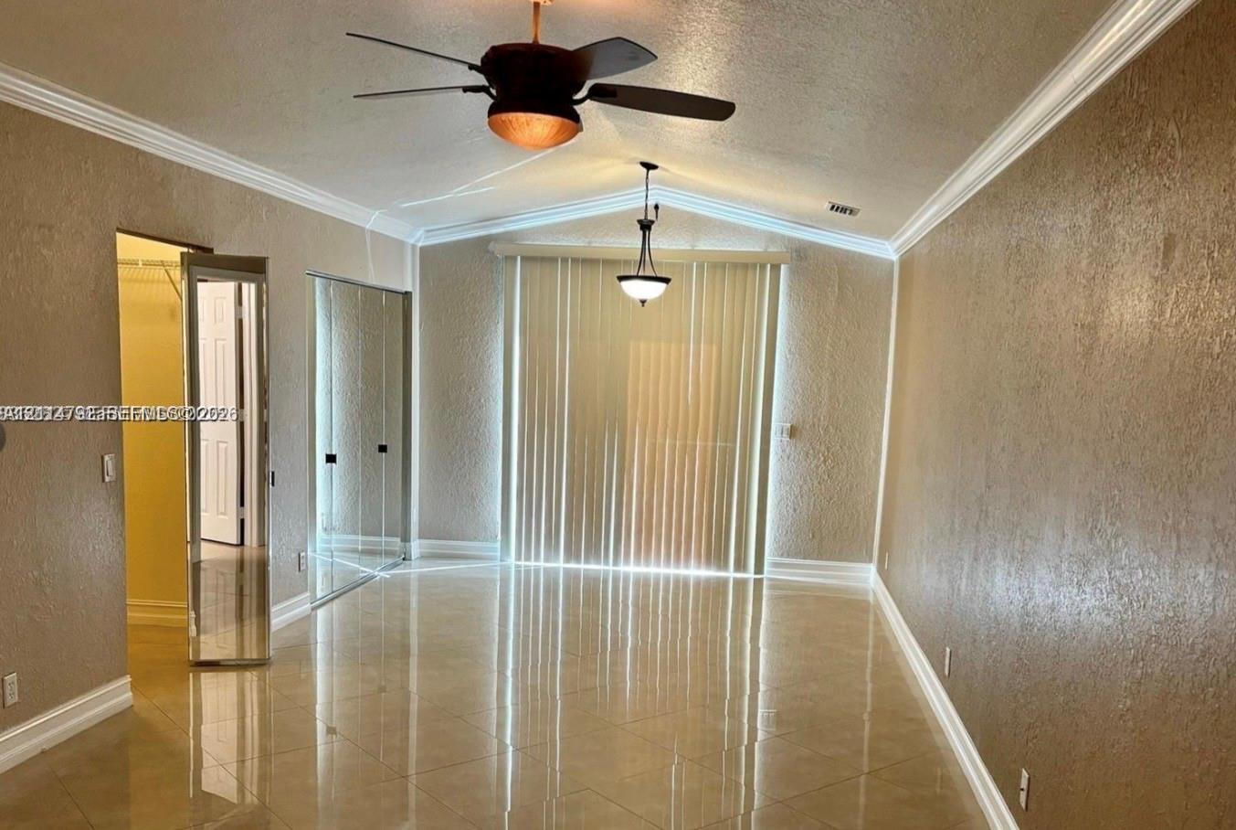 Vaulted ceiling featuring a central hanging light fixture and a multi-speed ceiling fan, neutral tile flooring, mirrored closet doors, and vertical window treatments