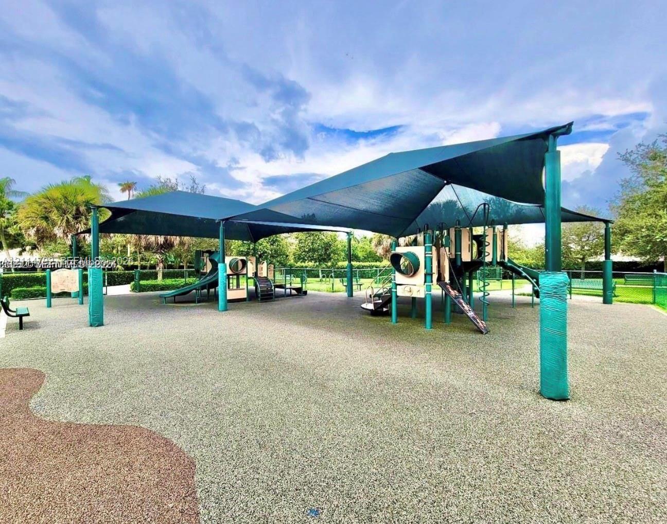 Recreational area featuring a large overhead tensioned canopy, multi-component play structure, rubberized surfacing, and perimeter landscaping