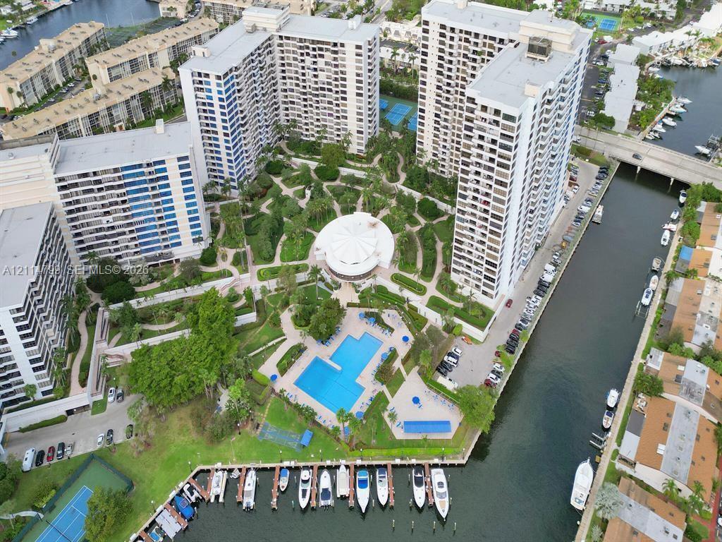 High-rise residential complex featuring a central swimming pool, landscaped gardens, tennis courts, and private boat slips along a waterway