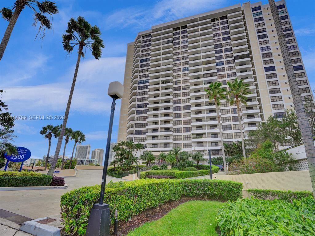 High-rise residential building featuring private balconies, expansive windows, manicured landscaping, and palm-lined exterior grounds
