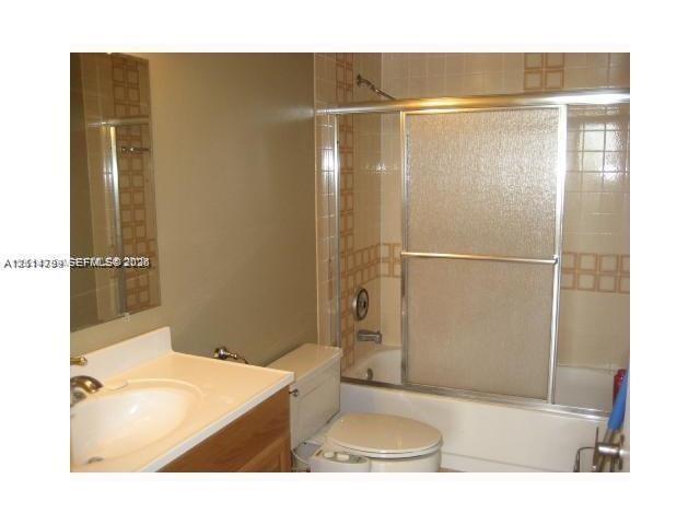 Bathroom featuring a wood-finish vanity, integrated sink, tub and shower combination with sliding glass doors, and decorative tile accents
