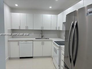 Kitchen featuring white flat-panel cabinetry, stone-finish countertops, stainless steel refrigerator, recessed lighting, and tile flooring