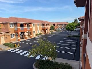 Stucco building exterior featuring arched entryways, tile roofing, and expansive paved parking area with marked stalls