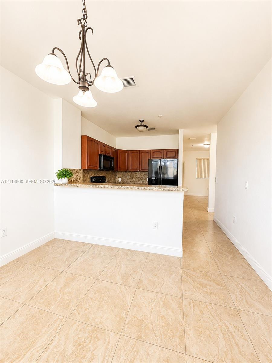 Kitchen featuring wood-finish cabinetry, stone-style countertops, tile flooring, and a decorative hanging light fixture